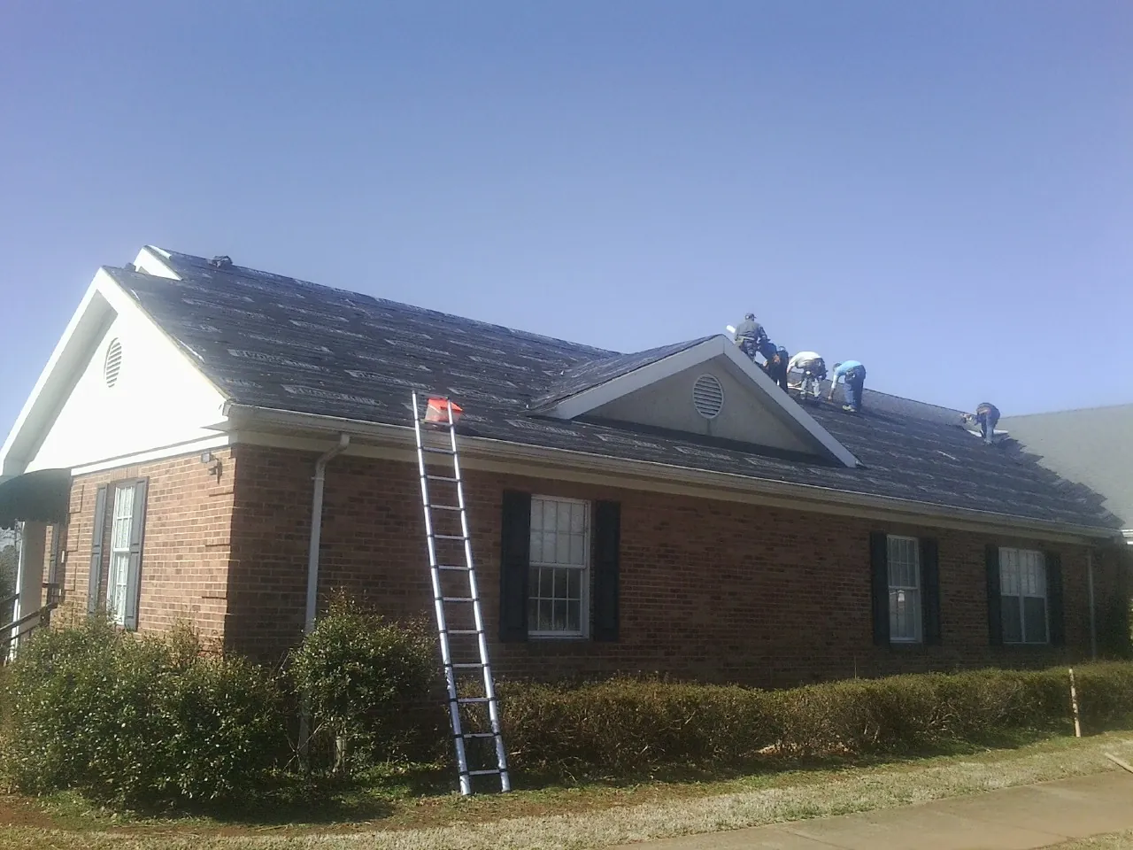 Crew tearing shingles off a brick ranch roof with a ladder set — Emergency Roof Repair work by our crew in Jenison