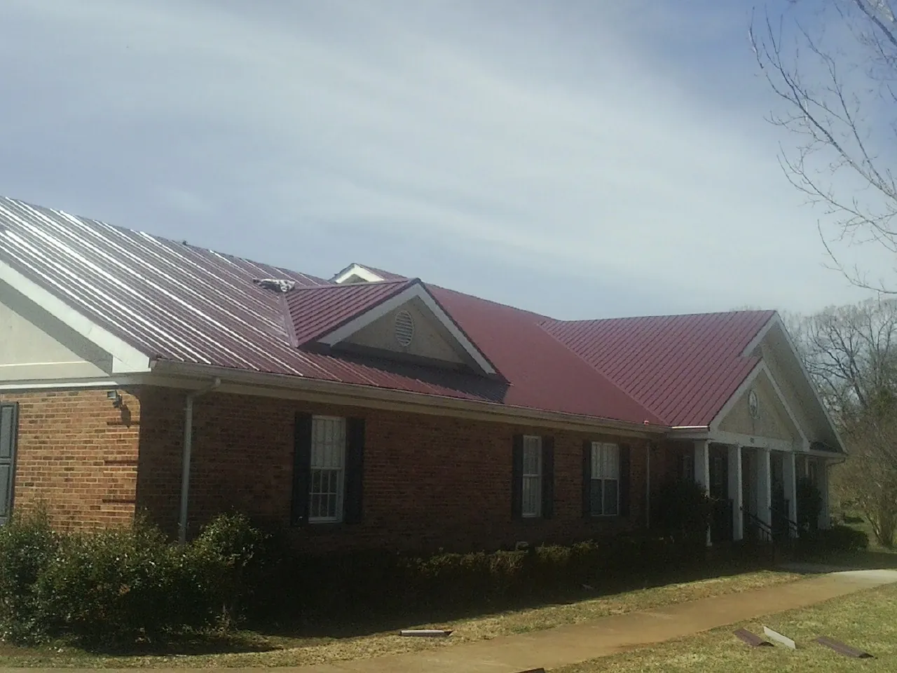 Red metal roof with gabled entries on a long brick building, from a Hail Damage Roof Repair job in Jenison