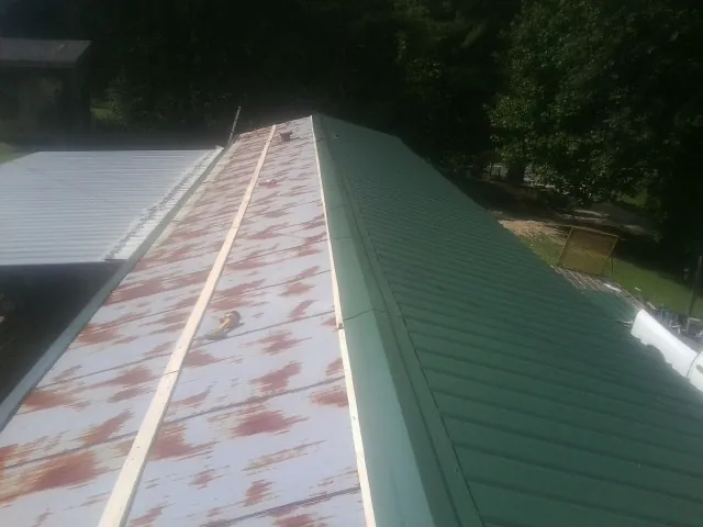 Old rusted panels beside newly installed green metal roofing — Wind Damage Roof Repair by Roofing Brothers in Jenison