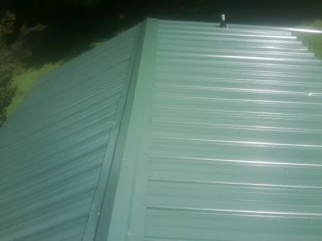 New green metal panels meeting at the ridge of a roof — Flat Roof Repair work by our crew in Jenison