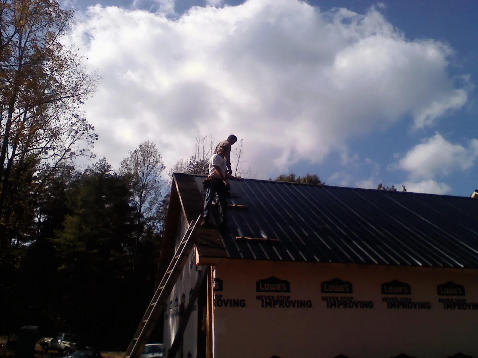 Roofer fastening dark metal panels high against a cloudy sky, from a Roof Inspection job in Jenison